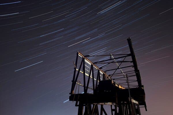 Streaks of light fly through a dark sky over a shadowed structure.