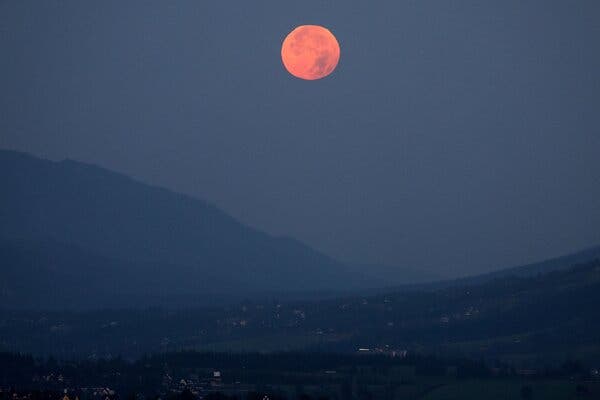 A red moon over some mountains on a dark day.