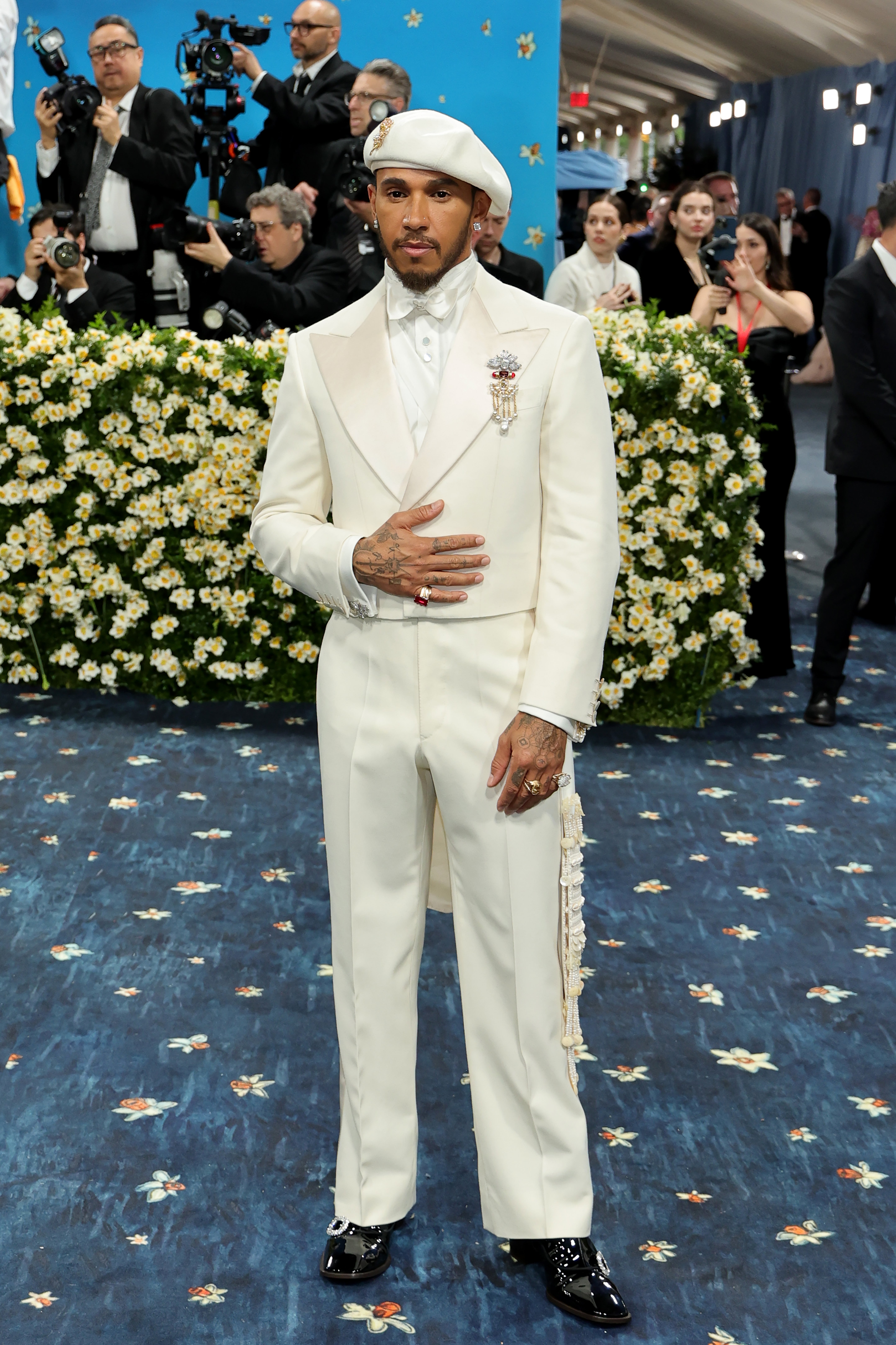 Lewis Hamilton stunned in a white tuxedo and matching silk bowtie. He had a silver and gold brooch attached to his jacket, as he completed his look with a white beret, diamond earrings, and gold rings