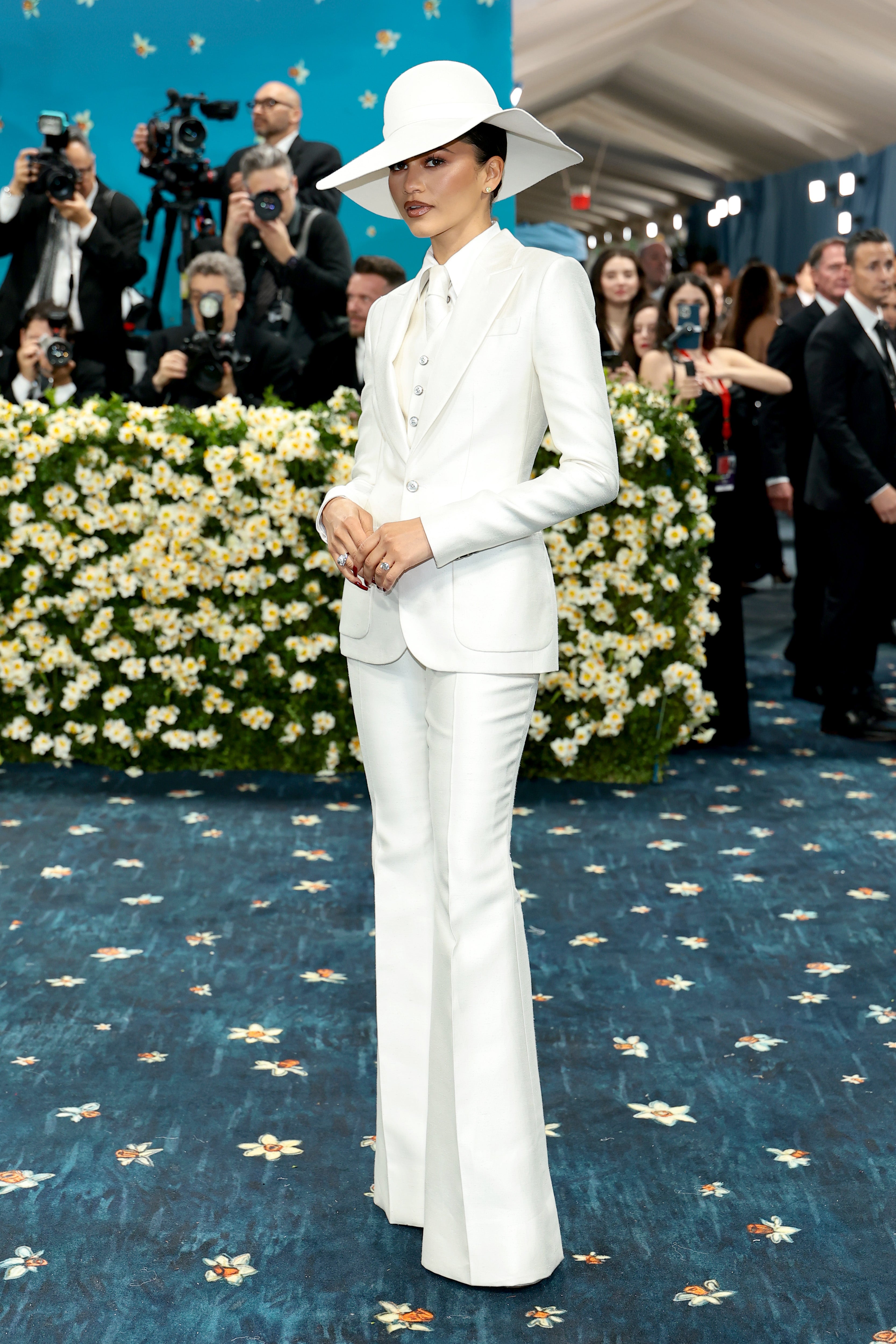 Zendaya wore an all-white tuxedo, featuring a matching tie and hat, by Pharrell Williams for Louis Vuitton. She completed the look with silver rings and earrings