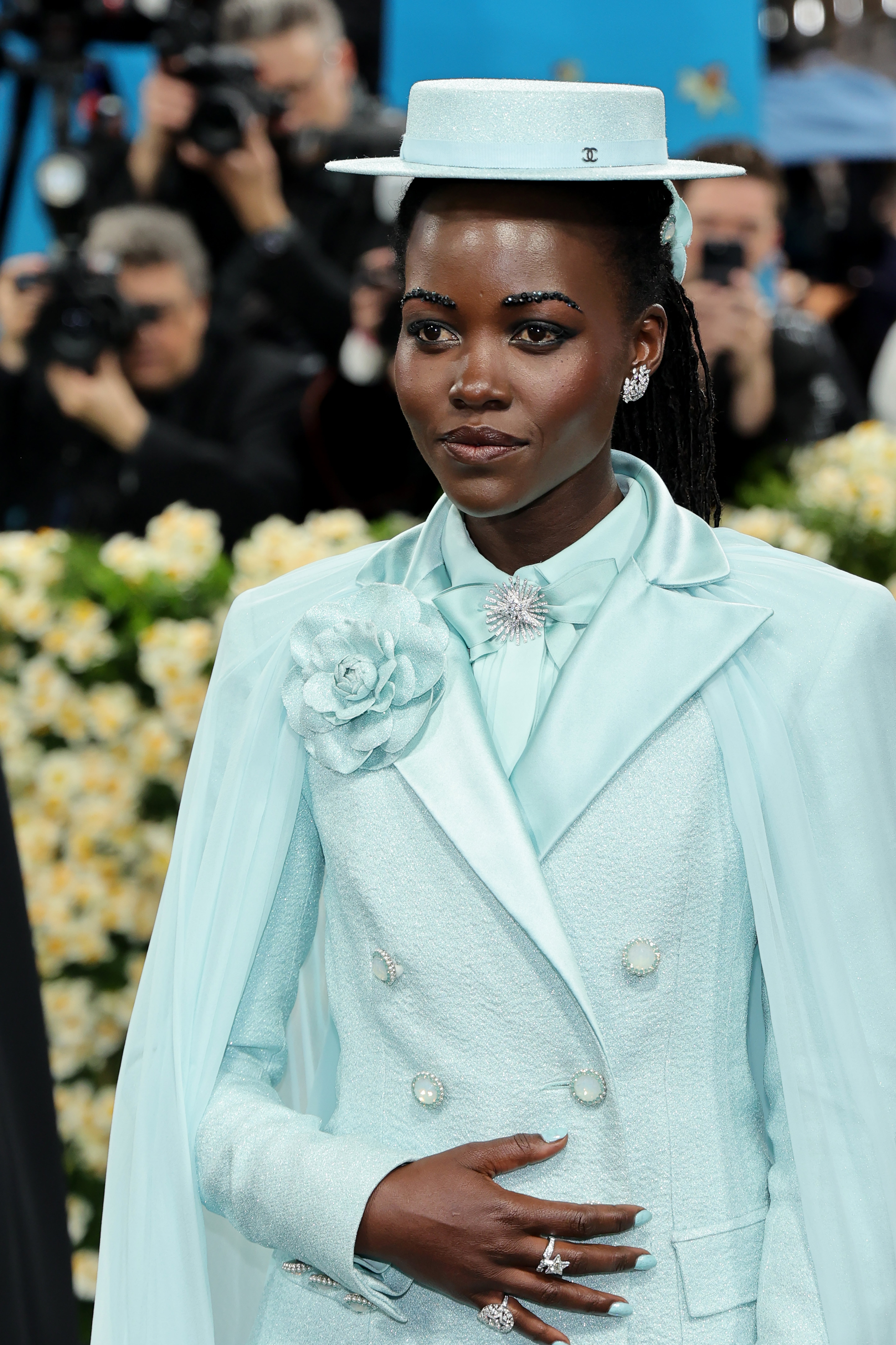 Lupita Nyong’o wore a powder blue suit by Chanel, along with a matching hat, silver earrings, a brooch in the middle of her shirt, and glitter on her eyebrows