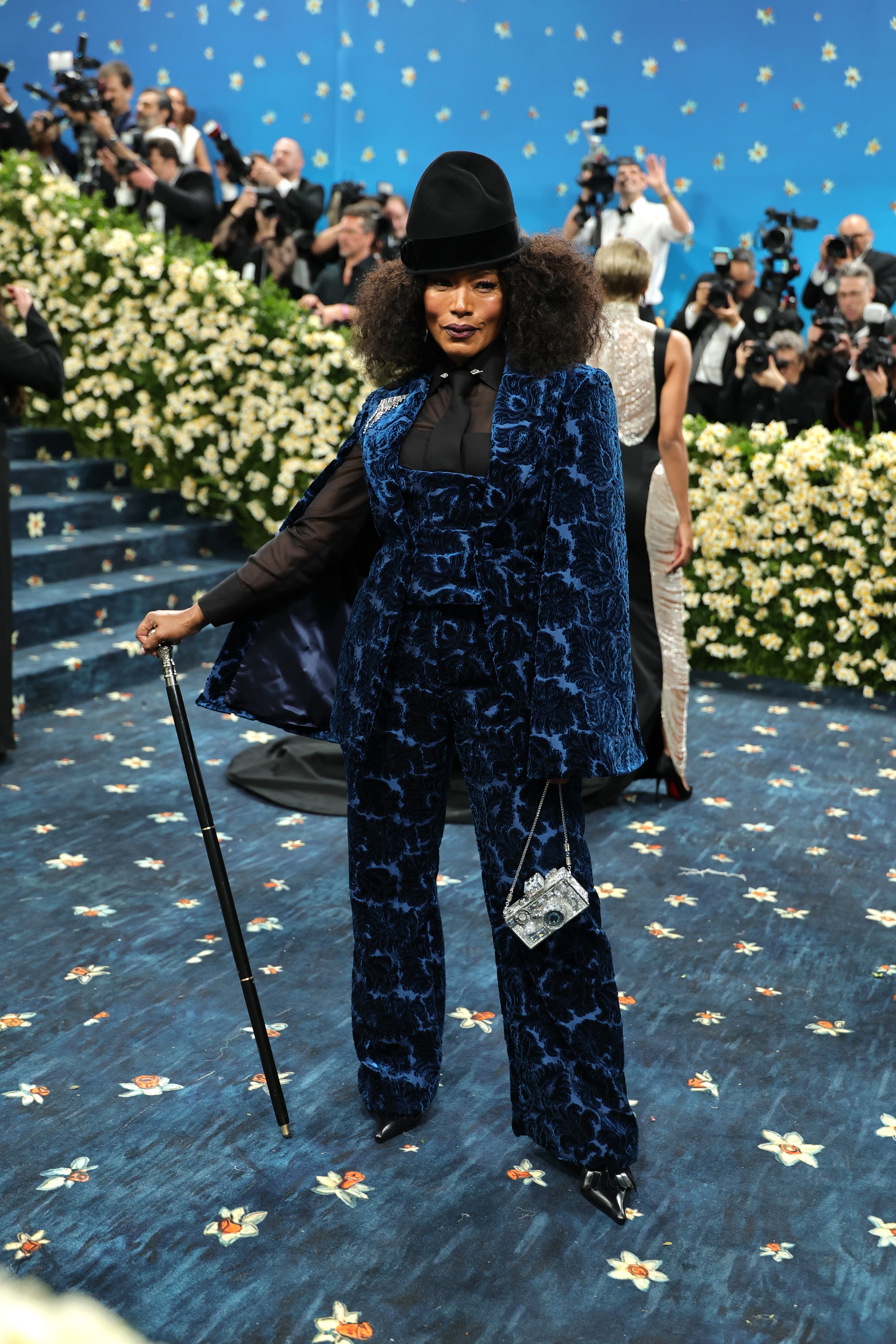 The actor had a black cane in hand and a silver square purse that looked like a camera