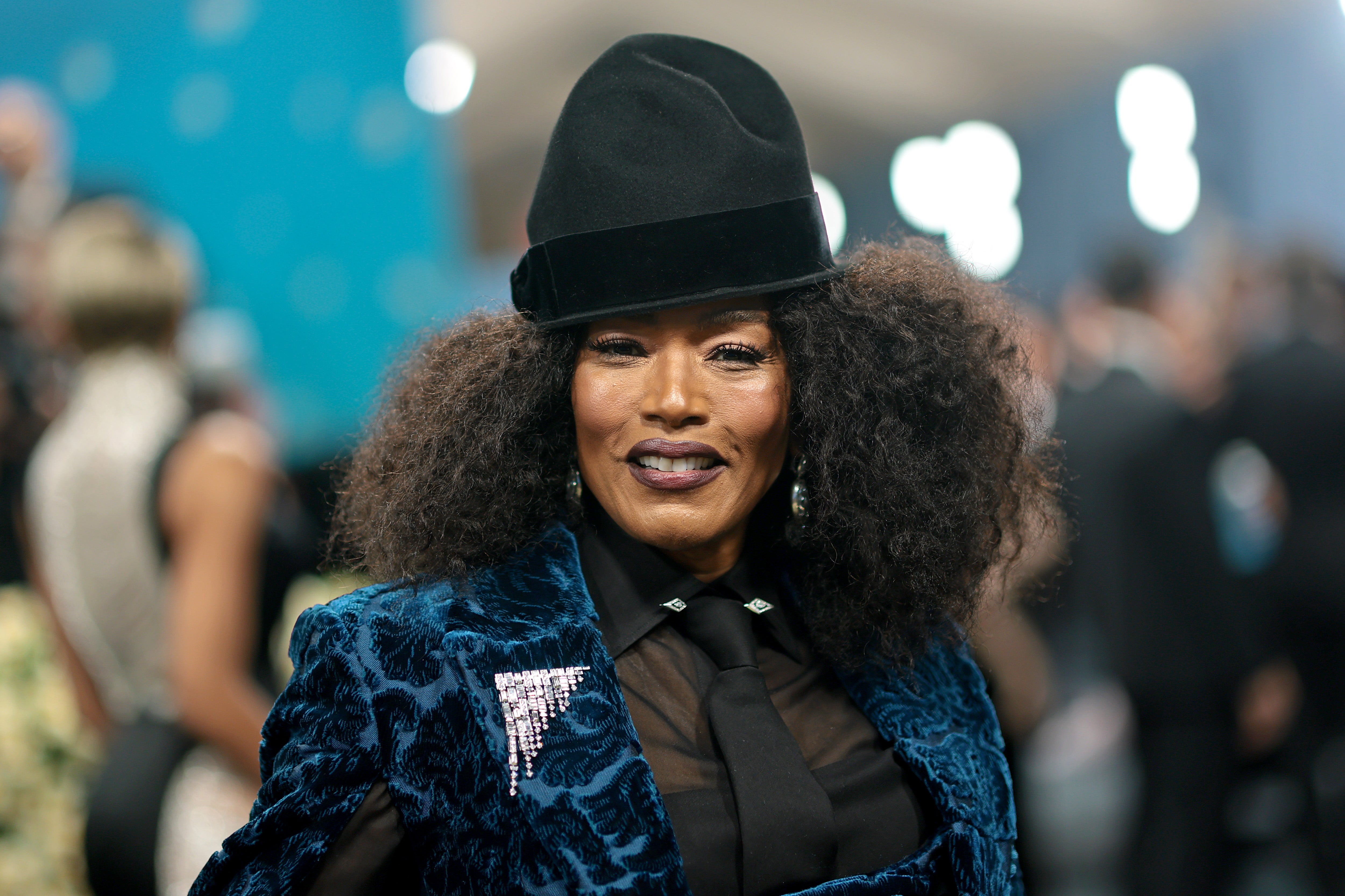 Angela Bassett arrived in a blue velvet pantsuit, sheer long-sleeved top, and a matching black tie. She capped off the loock with black top hat and a diamond pin on her jacket