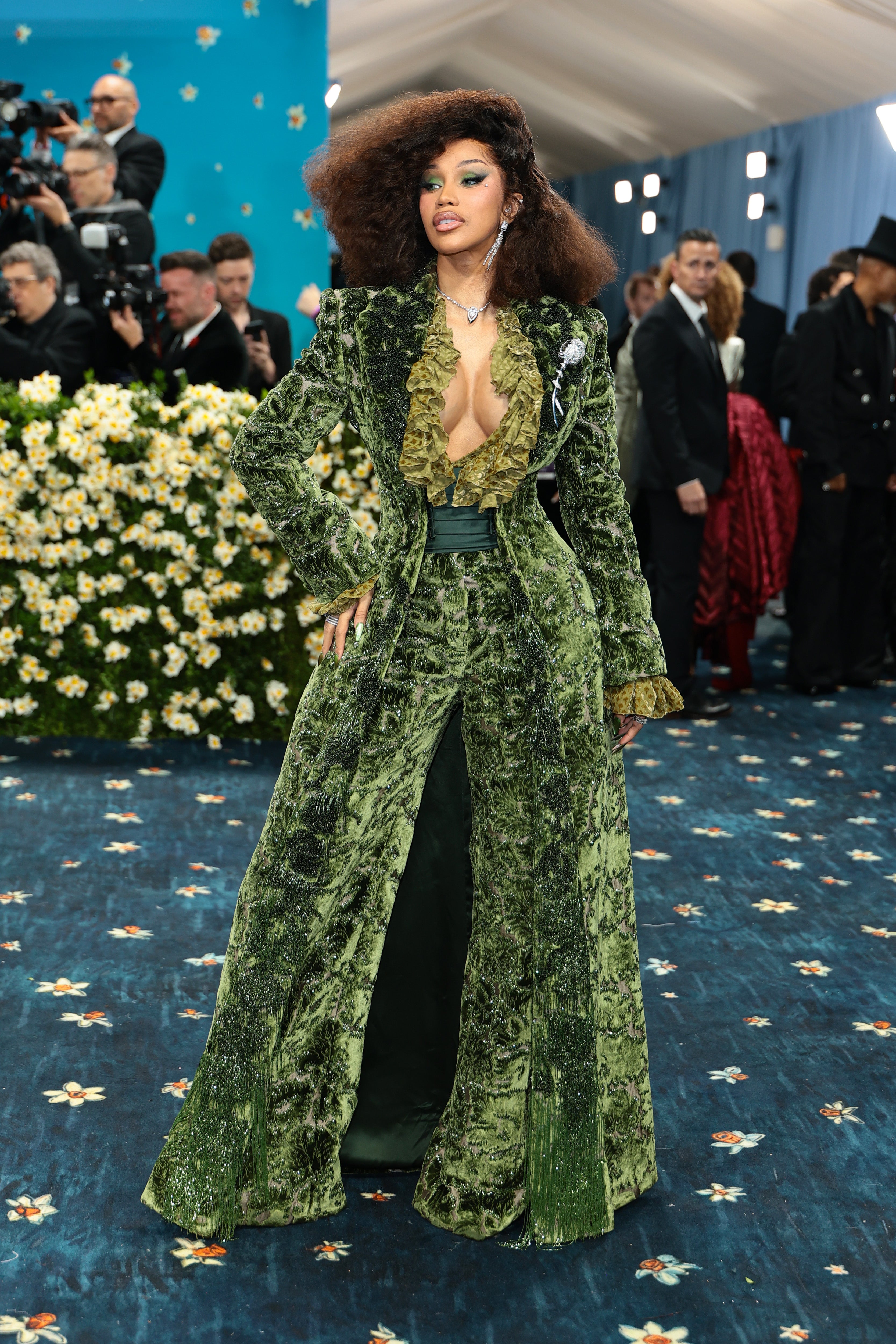 Cardi B wore a green pantsuit from Burberry featuring a low-cut neckline. Her look also included a dark green belt, with matching green eyeshadow and diamond earrings